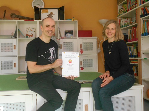 Foto: Kita-Leiter Dirk Schneeberg und Brit Ruschovy, Sprachfachkraft in der Kita, zeigen die Urkunde „Gütesiegel Buchkindergarten“